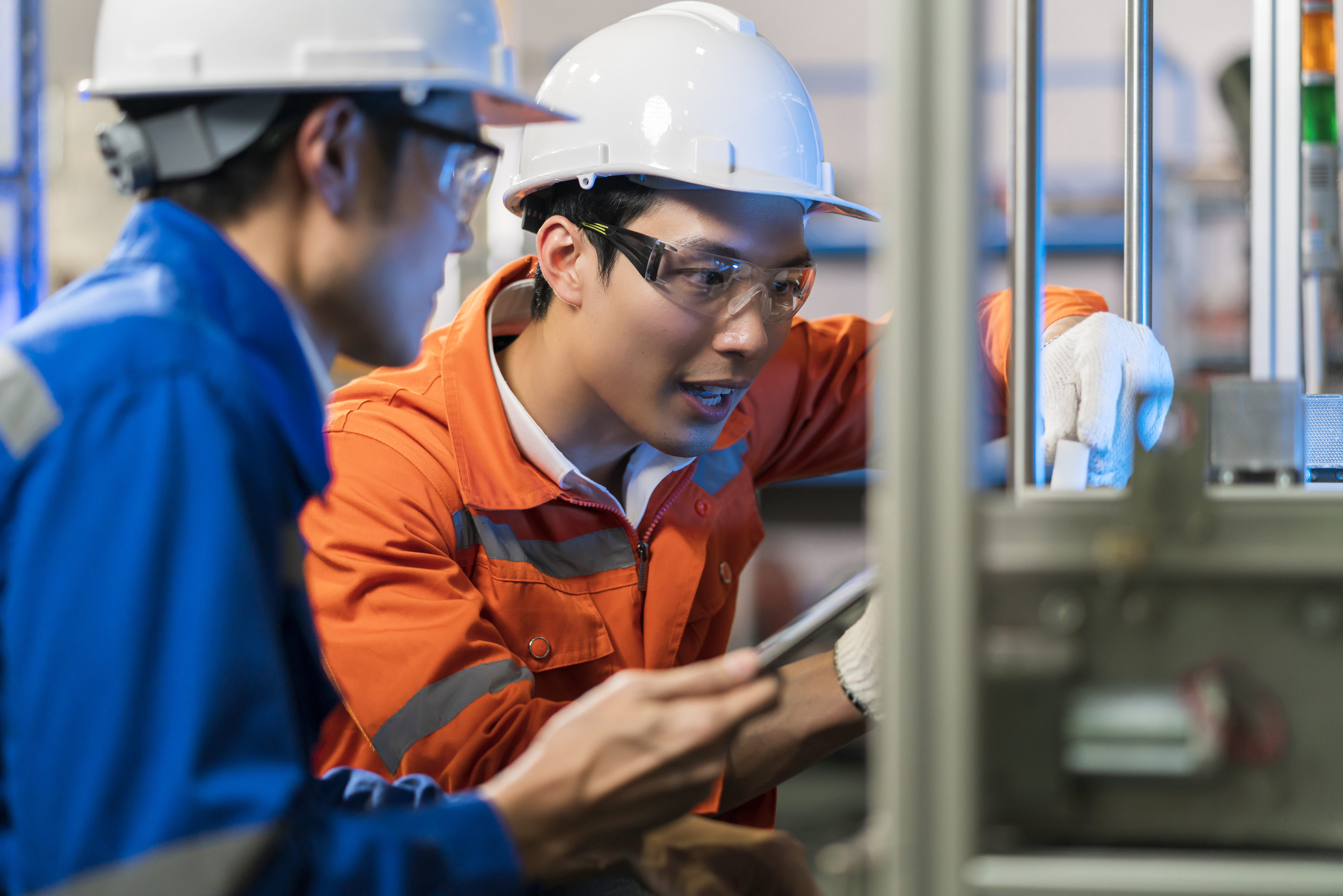 Male Asian engineer professional having a discussion standing by the machine in the factory ,two asian coworker brainstorm explaining and solves the process curcuit mother board of the machine
